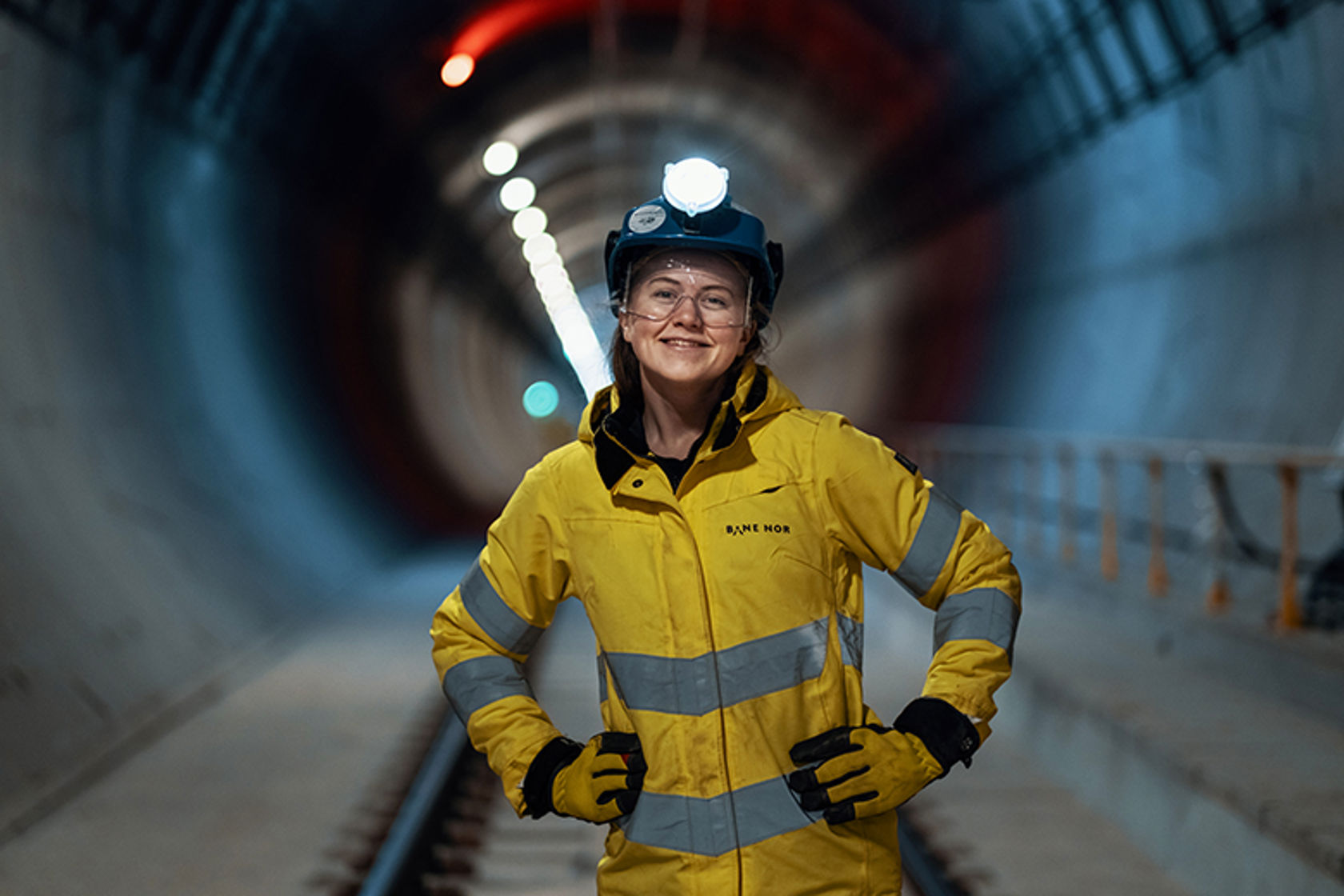 Bild kvinne i arbeidsklær inne i en tunnel. 