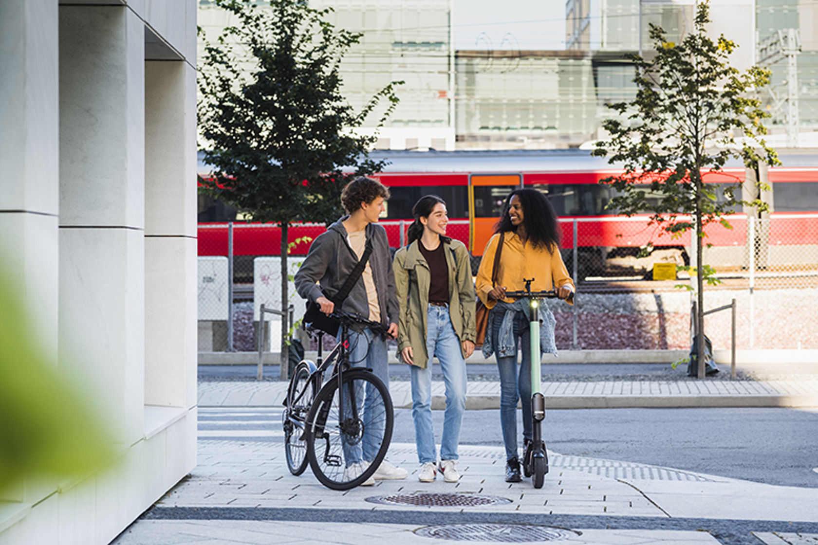 Ungdommer til fots, med sykkel og sparkesykkel går på en togstasjon.