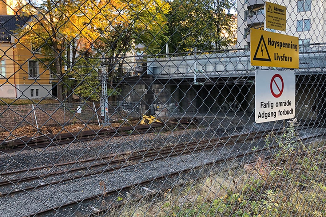 Bildet viser et gjerde som gjerder inn et jernbaneområde med skinner og tunnel. 