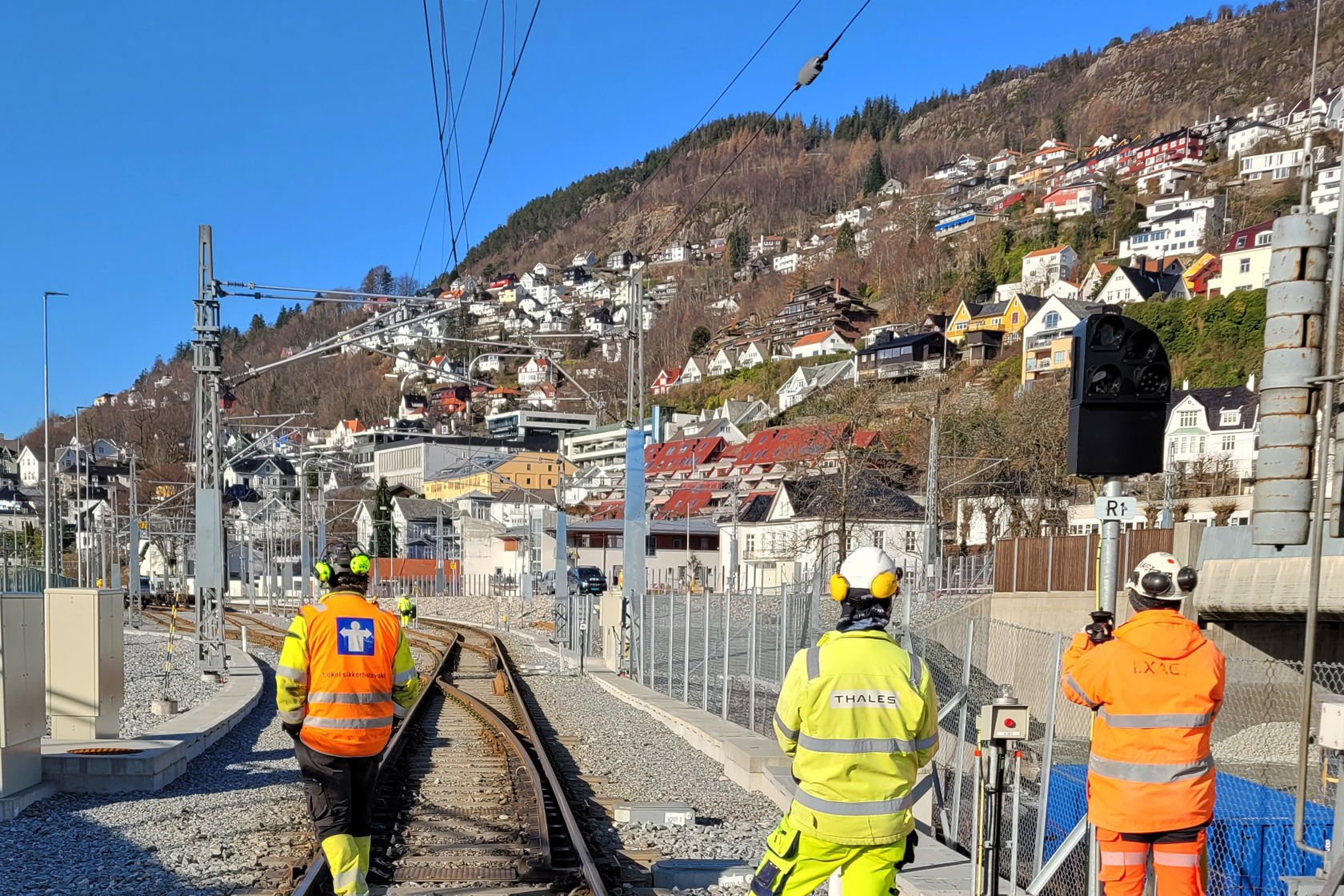 Tre mann i gult vernetøy skodar utover spora på jernbanen nær Bergen stasjon.