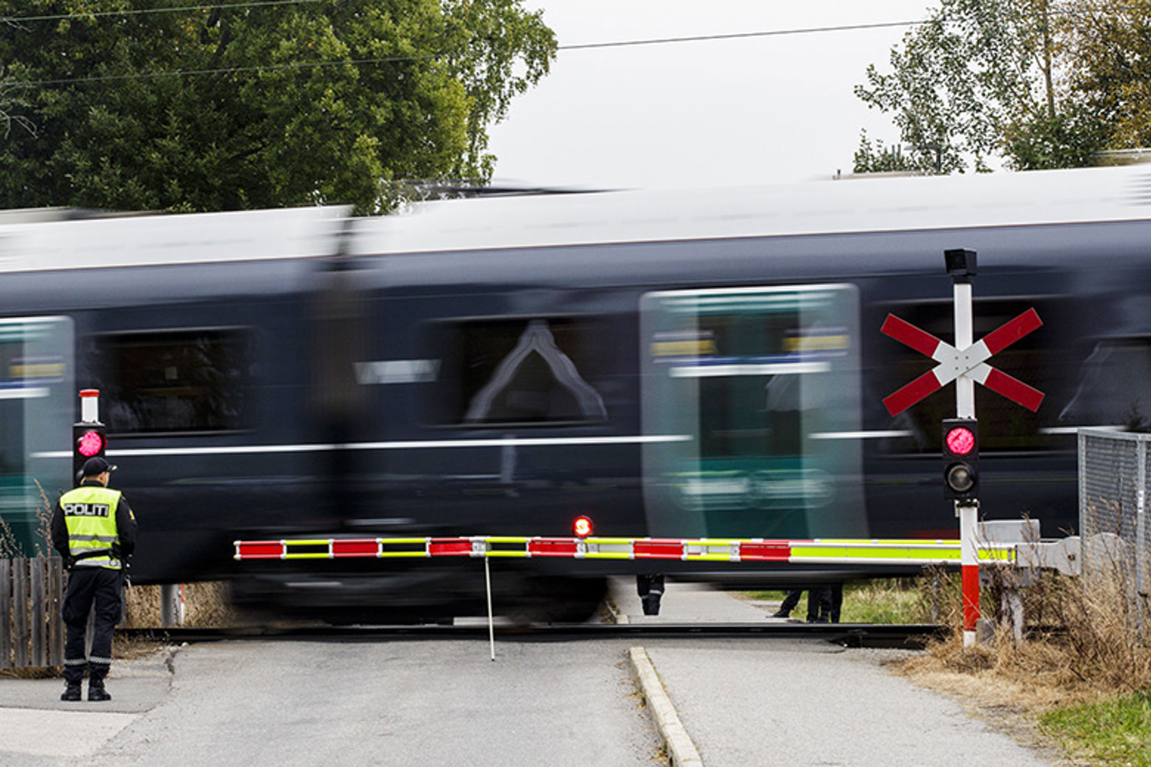Et tog kjører i full fart over en planovergang. Sikkerhetsbommene ligger nede