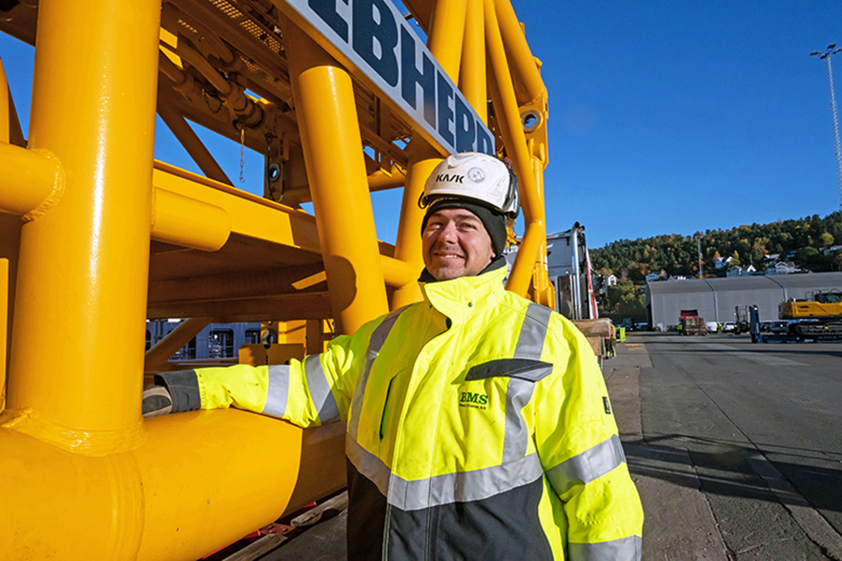 Mann i hjelm og gule arbeidsklær stående ved en gul maskin.