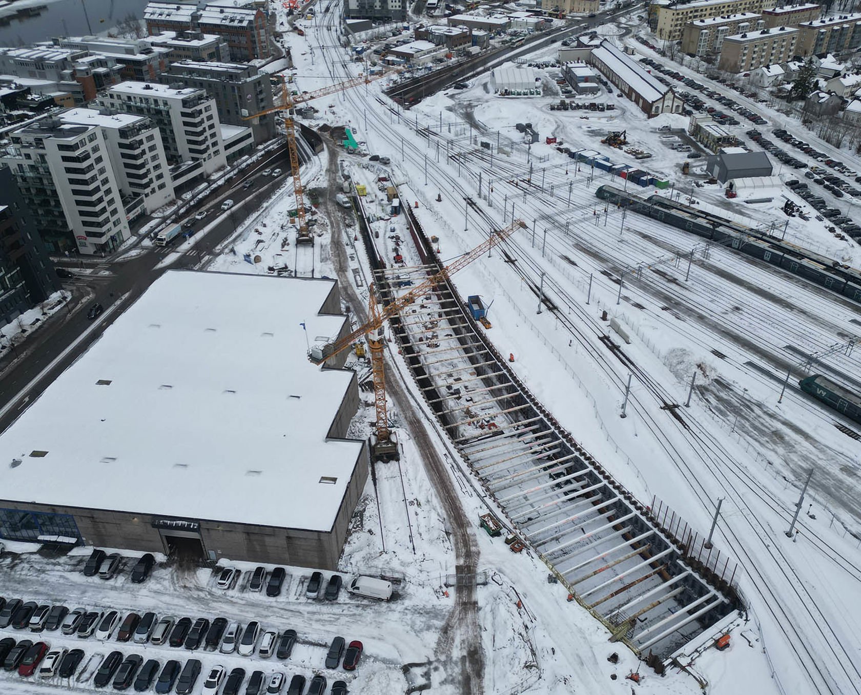 Byggeplass nær togspor med kraner og snø.