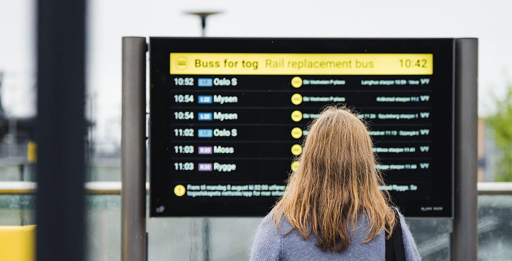 Reisende ser på monitor med avgangstider for buss for tog.