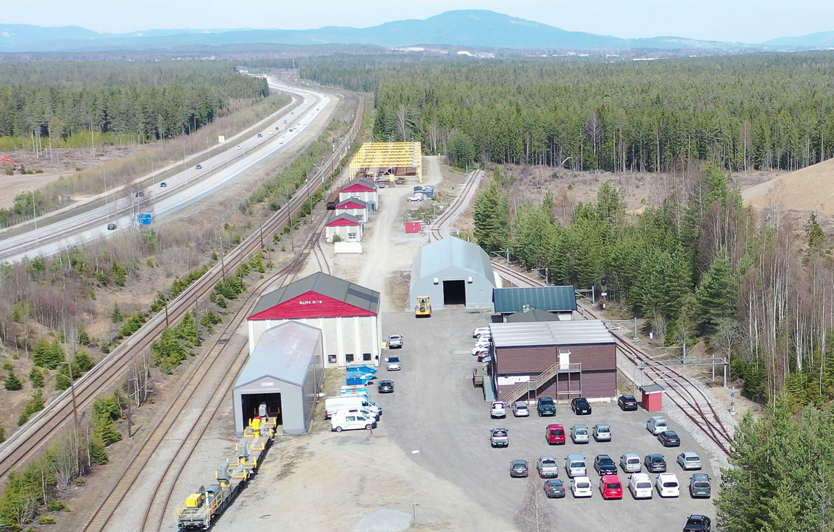 Dronefoto med skinnelageret i forgrunnen, Hovedbanen og E6.