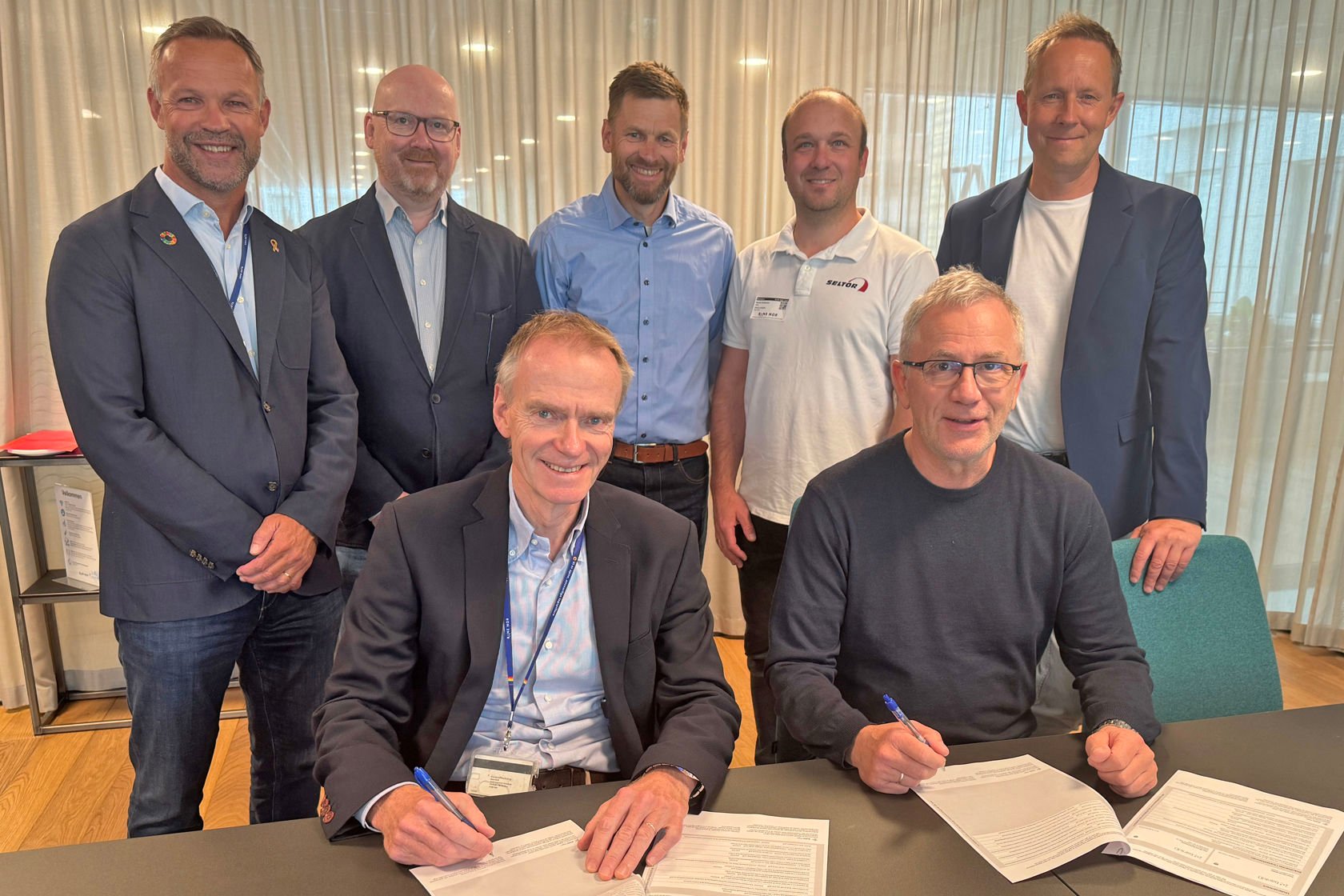 De to som signerer kontraktene sitter foran, mens de andre står i en halvsirkel bak.