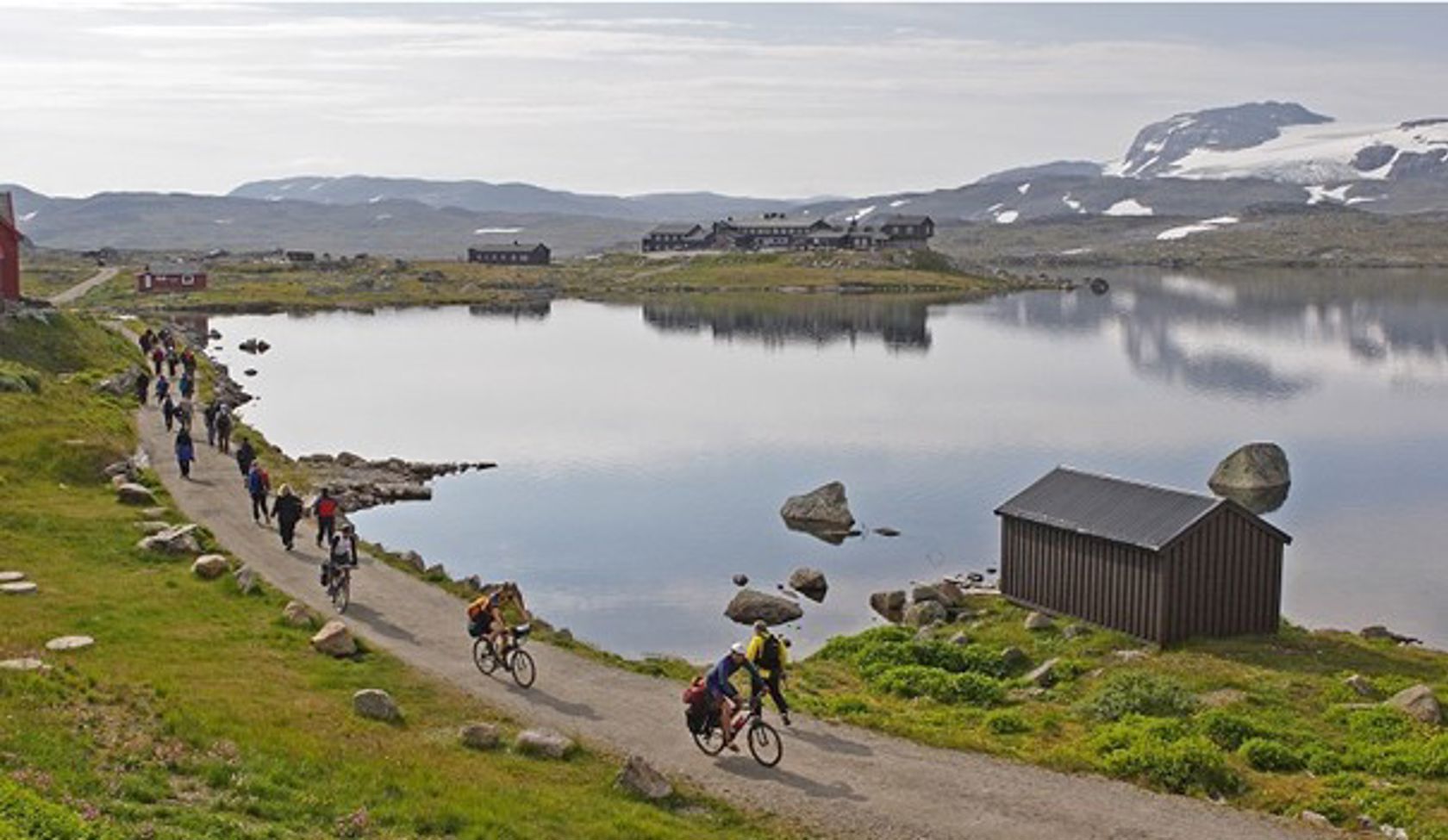 Utsynsbilete langs Rallarvegen med syklistar langs eit fiskevatn.