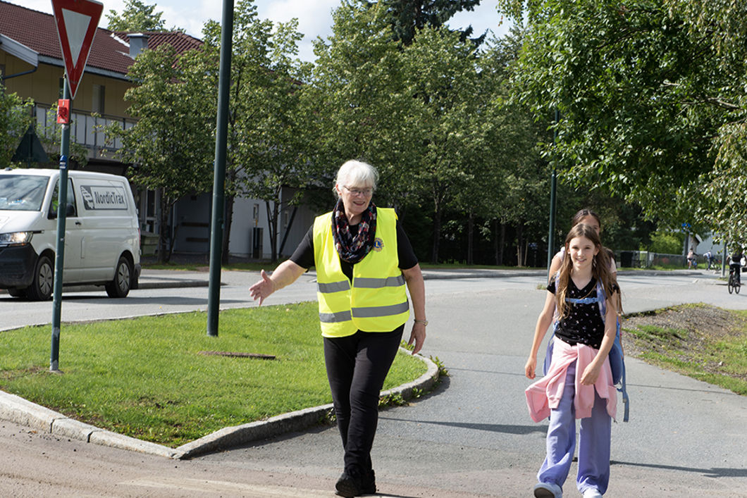 Kvinne i gul vest hjelper barn over veien.