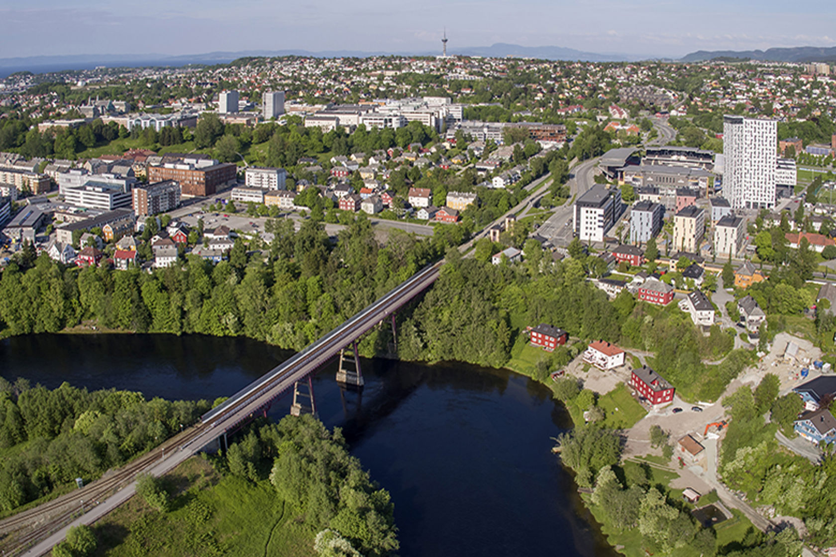 Oversiktsbilde over en del av Trondheim, med elv, bru, grønn park og bolighus