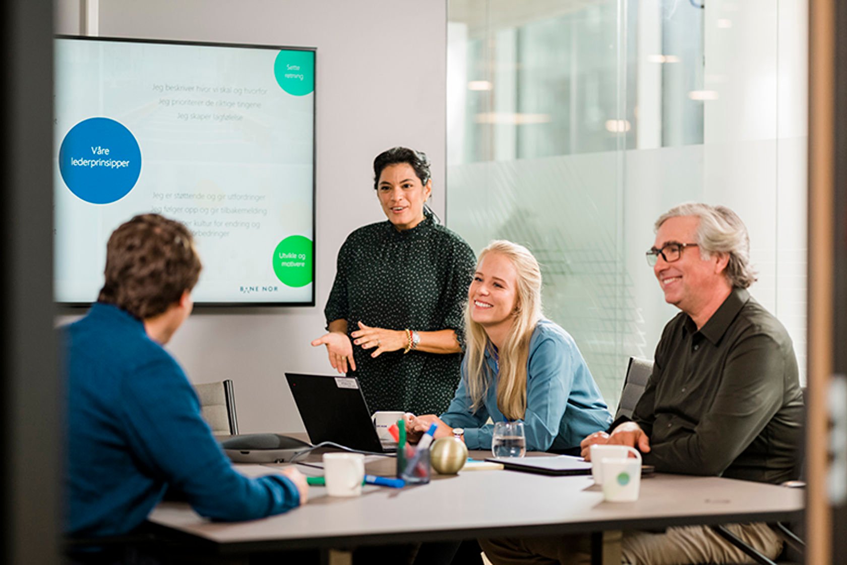 A person is showing a presentation on a screen. Four people are in the room.