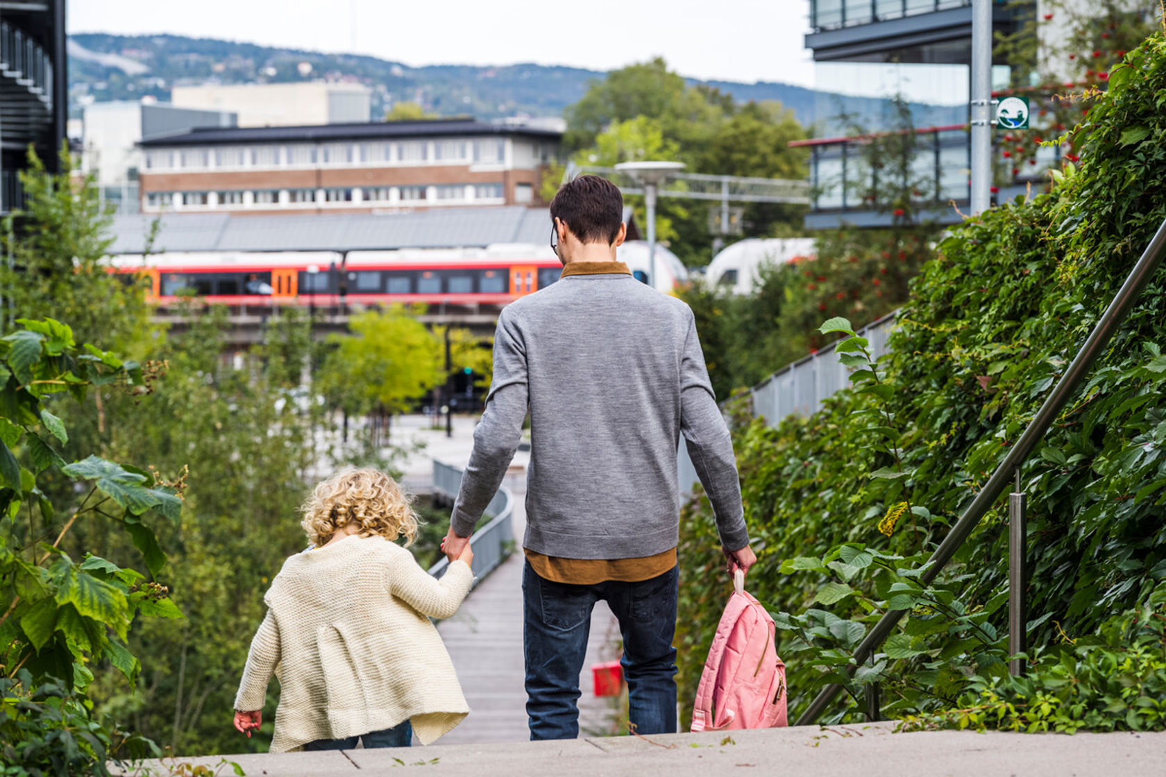 Bilde av en mann som leier en liten jente ned en trapp. Vi ser et tog i bakgrunnen.