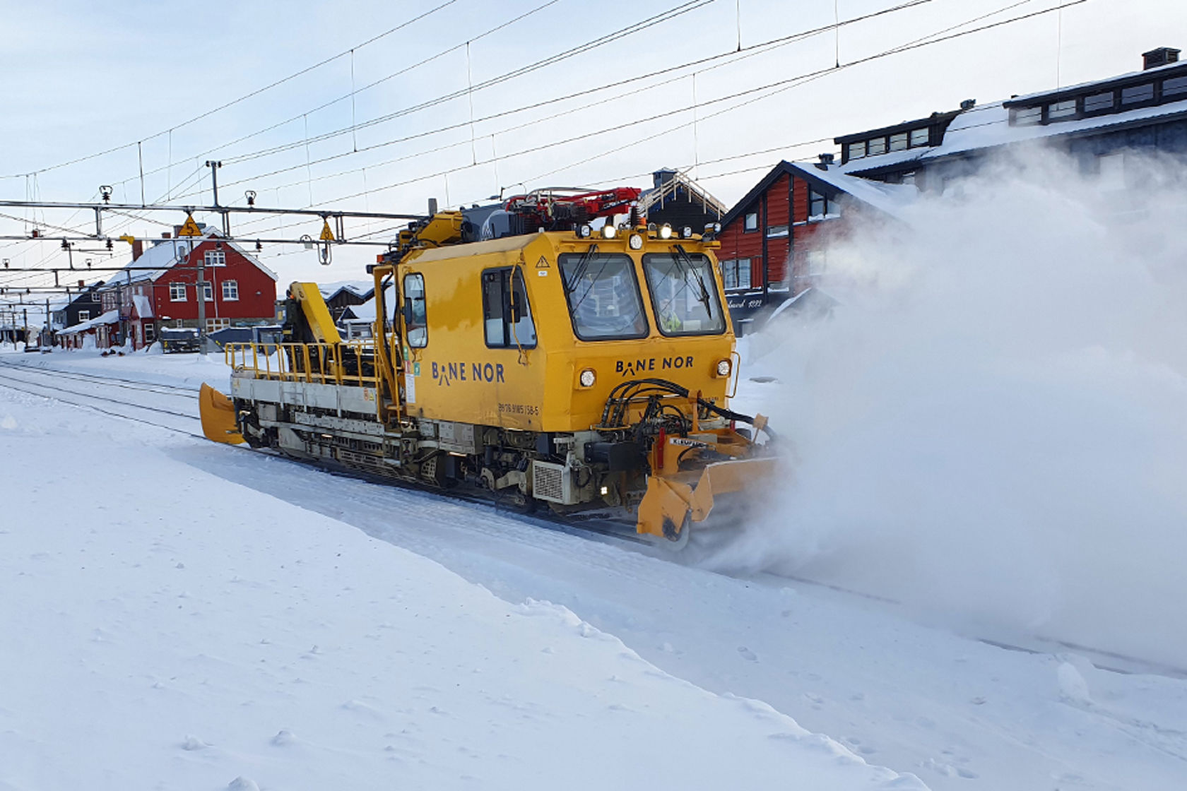 Bilde av en stor gul maskin på jernbaneskinner som brøyter og måker så snøføyka står.