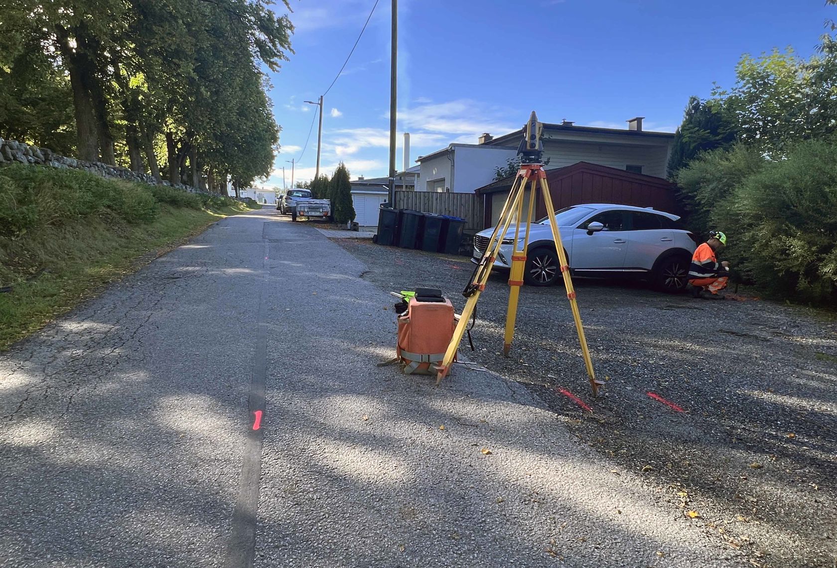 Vei med merking og måleapparat. I bakgrunnen står en bil og hus. 