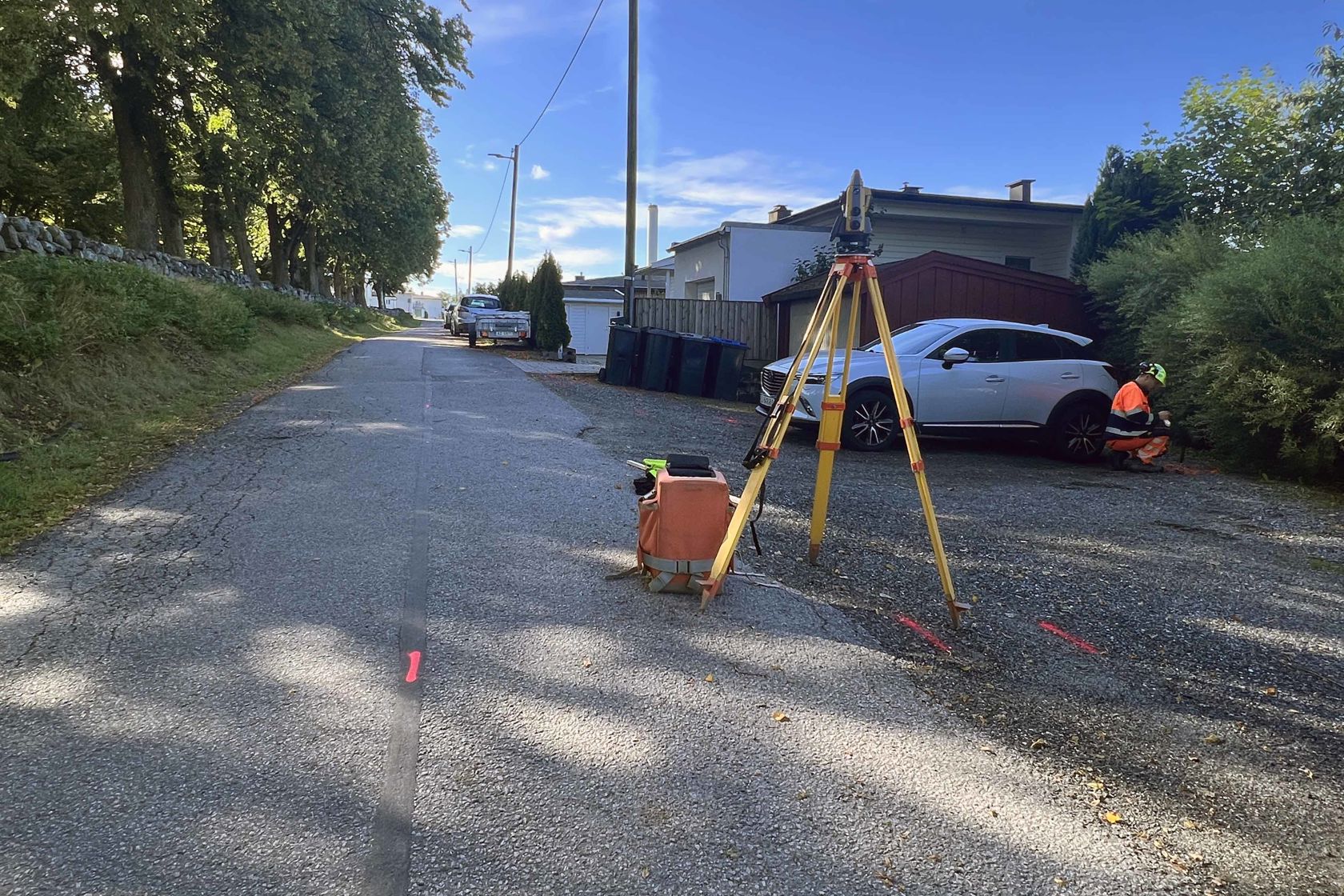Vei med merking og måleapparat. I bakgrunnen står en bil og hus.