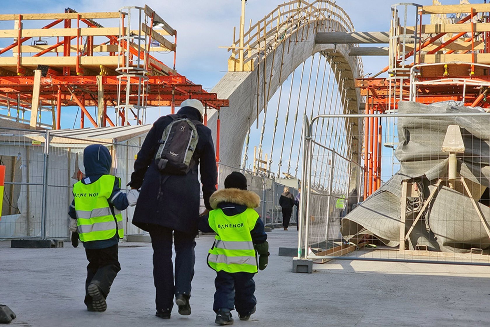 En voksen leier to småbarn med Bane NOR-vest ute på brua