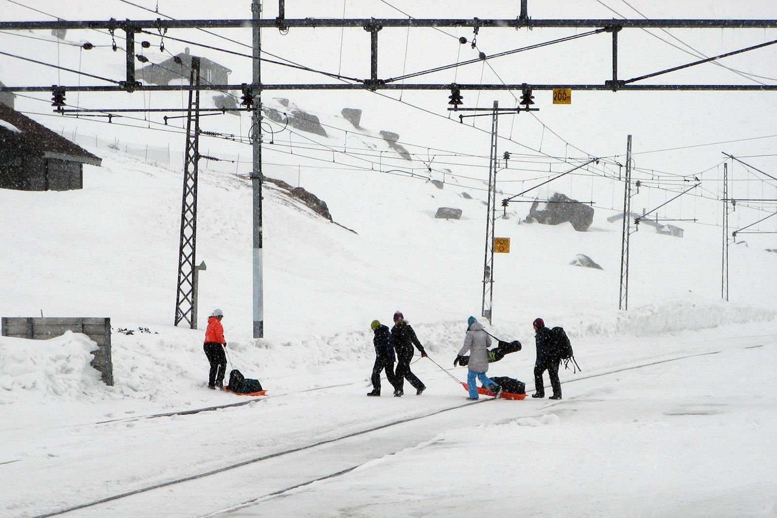 Fem personer med bagasje trekker oppakning over sporet på pulk/akebrett.