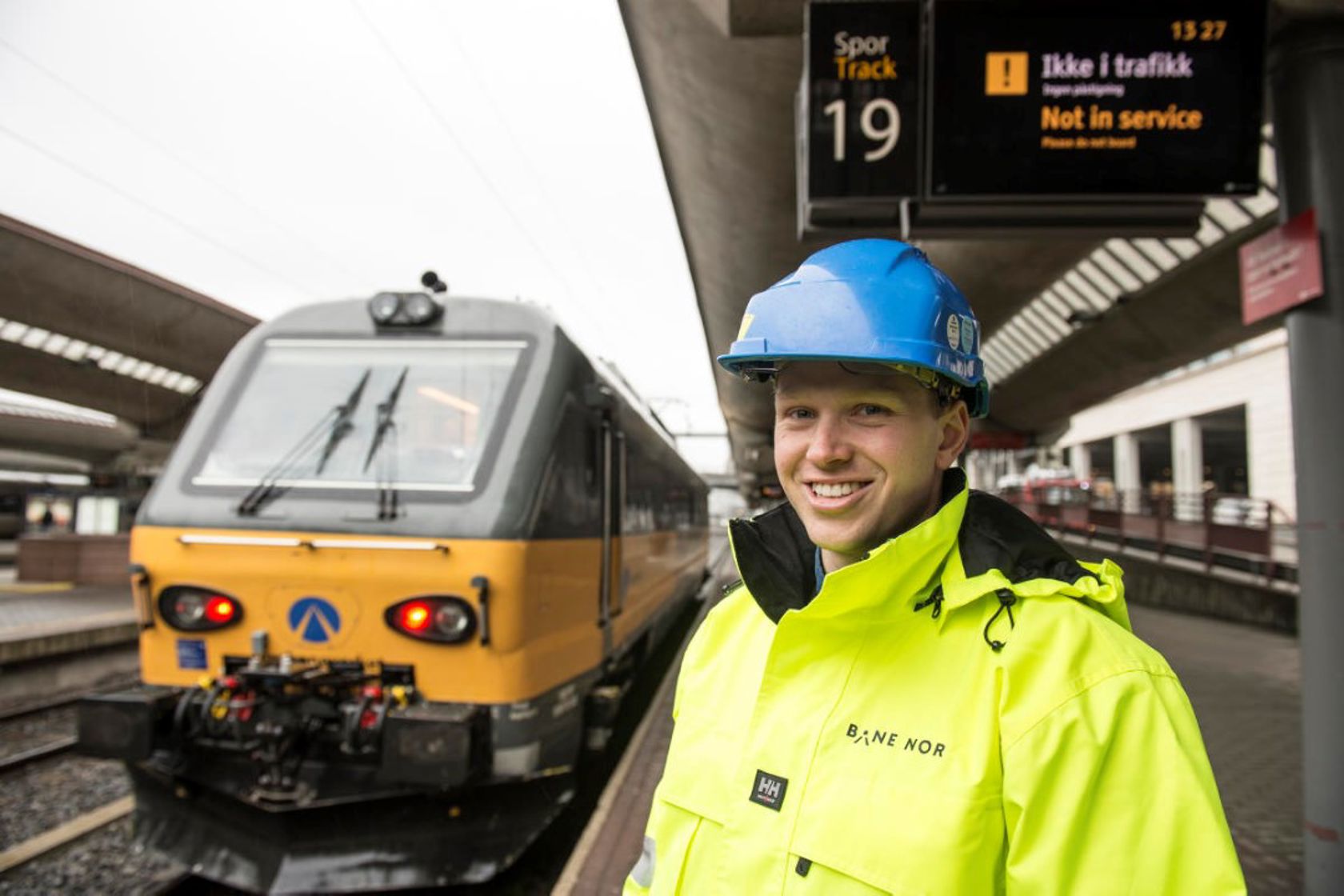 Portrettbilde av Jørgen Retvedt som står på et stasjonsområde, med et tog i bakgrunnen.