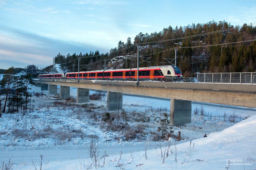 Tog kjører over jernbanebru gjennom snøkledd landskap