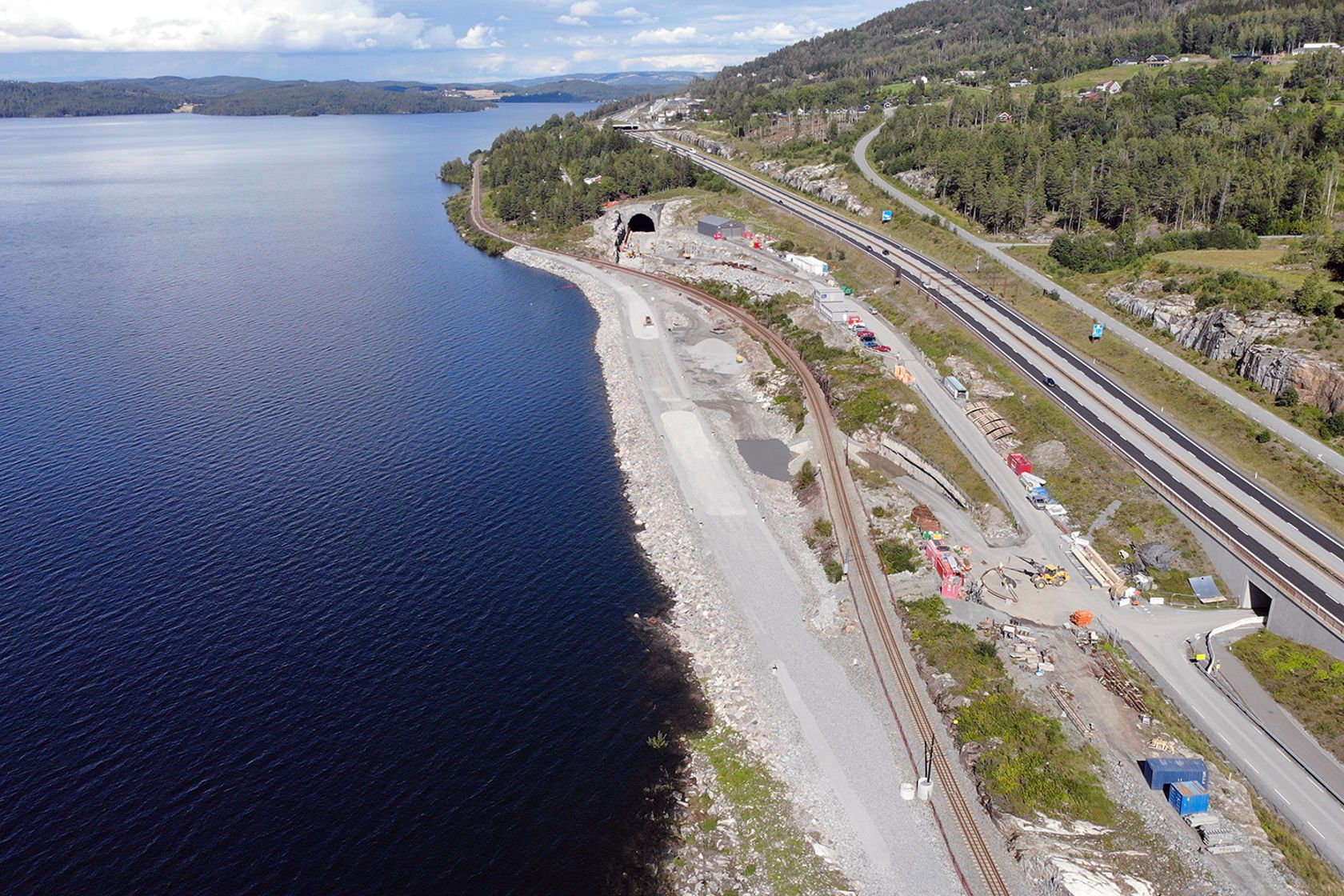 Dronefoto av Mjøsa, ny fylling og dagens jernbanespor, samt E6 og munningen av Hestnestunnelen.