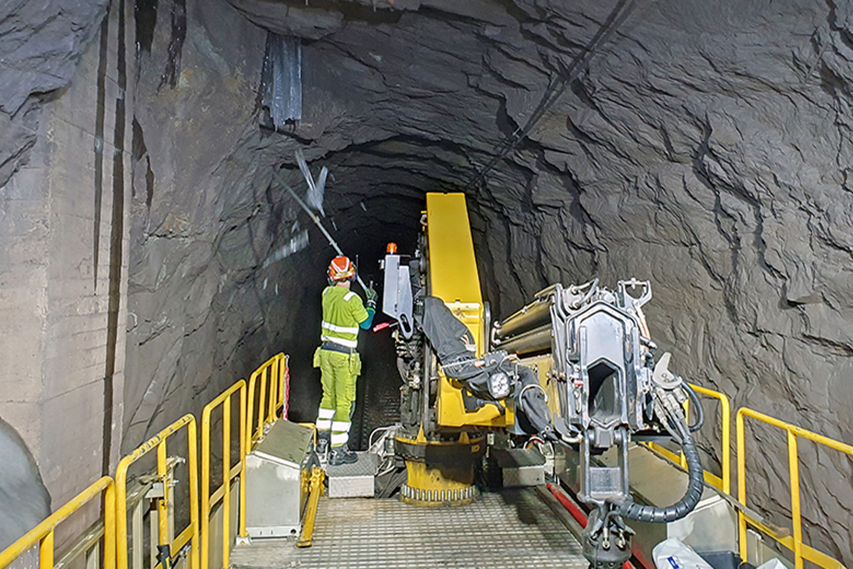 En mann står bakerst på et arbeidstog i tunnel og slår ned istapper fra tunneltaket.