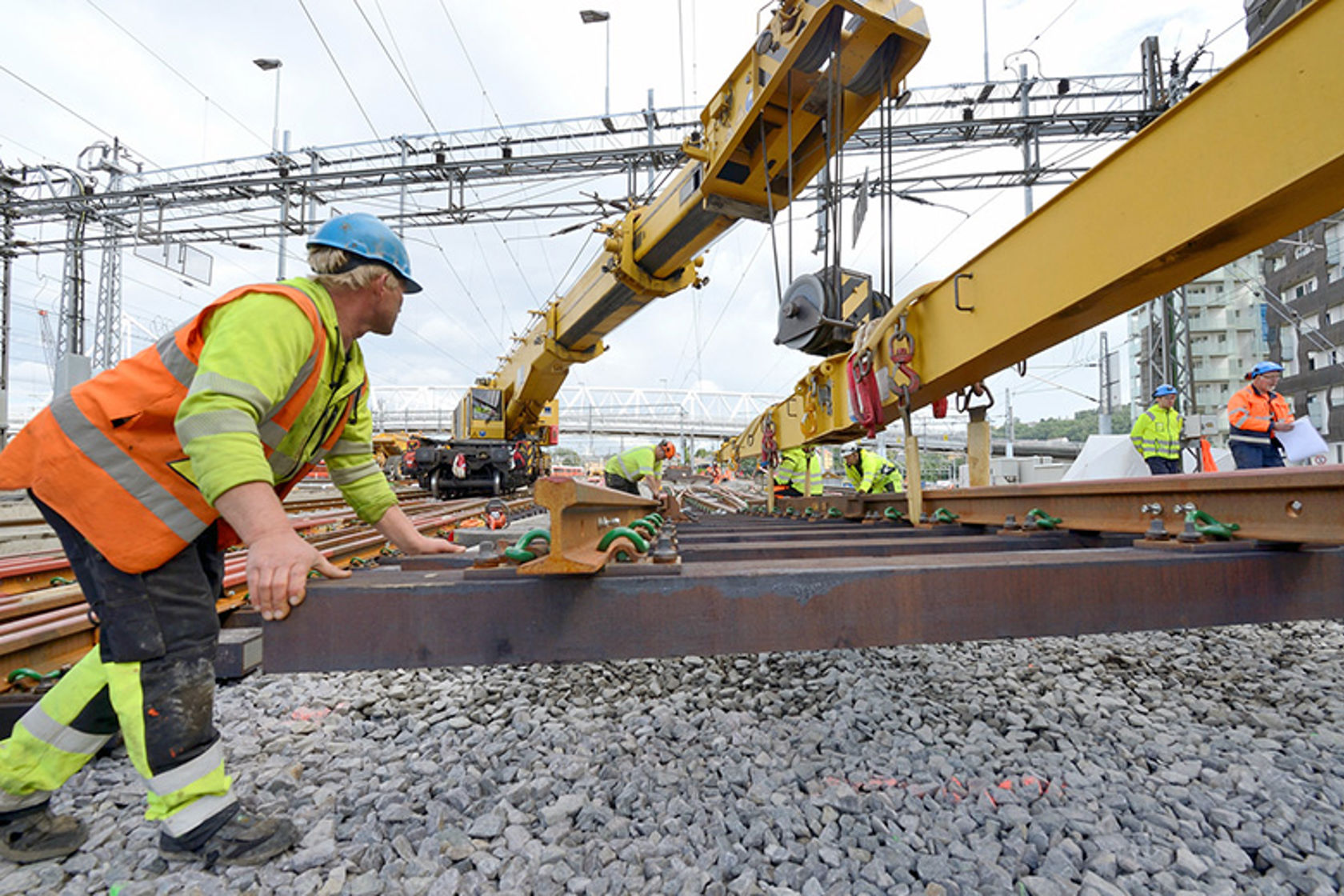 Anleggsarbeidere løfter på plassjernbaneskinner ved hjelp av kran