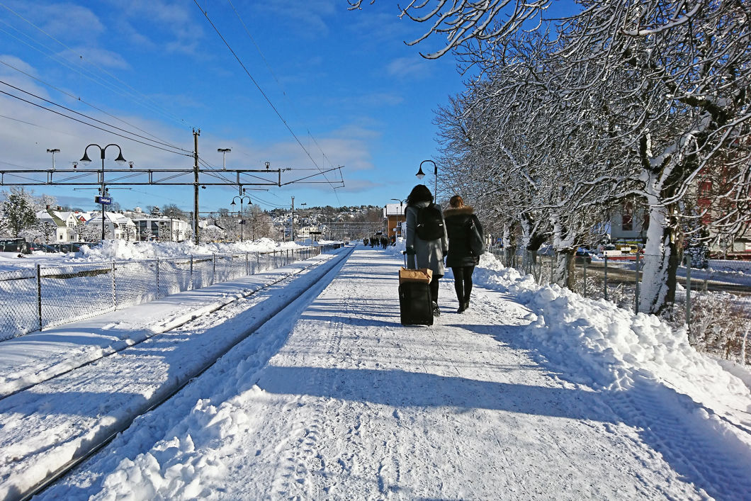 To kvinner med trillebagar går opp på ei snødekt plattform for å reisa med toget.