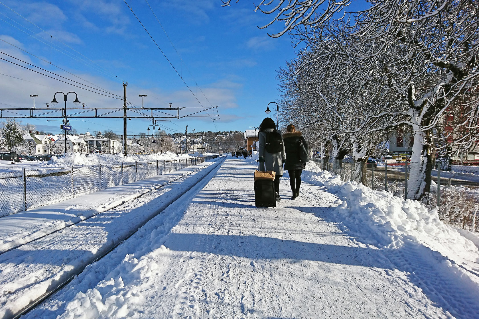 To kvinner med trillebagar går opp på ei snødekt plattform for å reisa med toget.