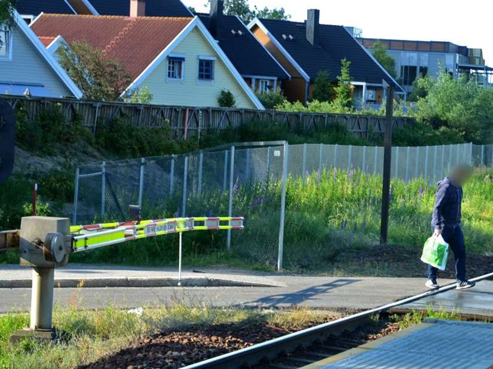 En person går over togets skinnegang mens bommen ligger nede.