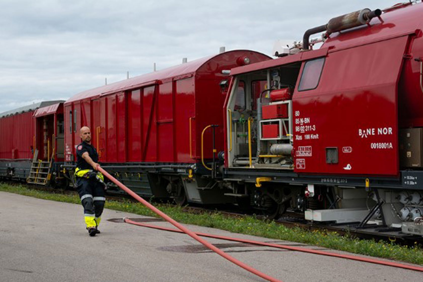 Bilde av en brannmann som holder en brannslange, med et rødt tog i bakgrunn.