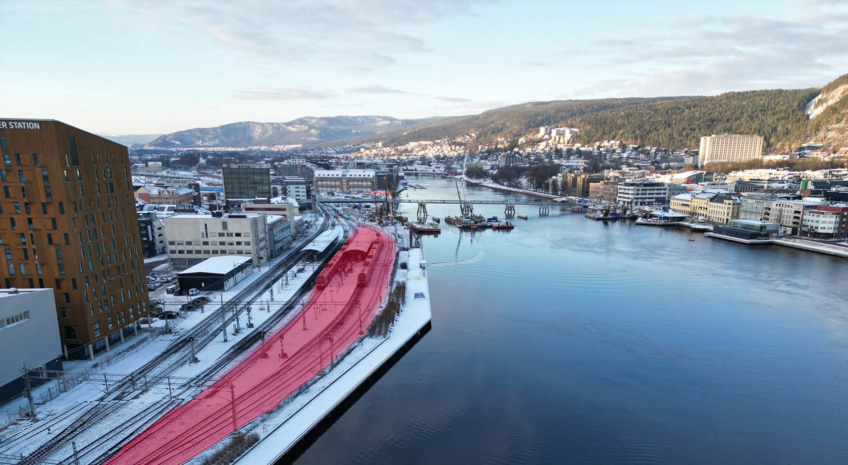 Oversiktsbilde over Drammenselva , stasjonen og deler av byen sett fra øst. Sporområde markert med rødt. 