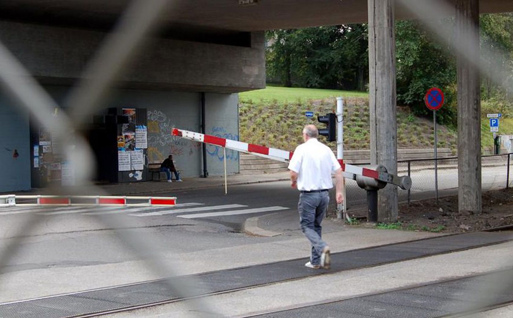 En mann er på vei gående mot en planovergang der bommene går ned.