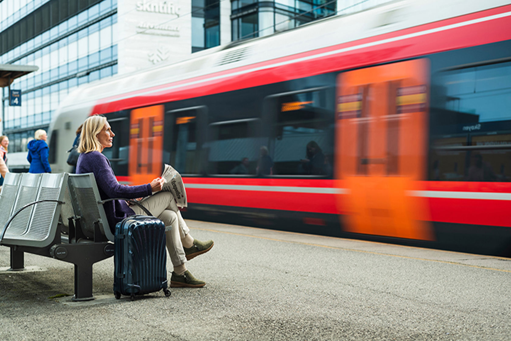 Kvinne sitter på en benk på en togplattform og ser et tog kjøre forbi