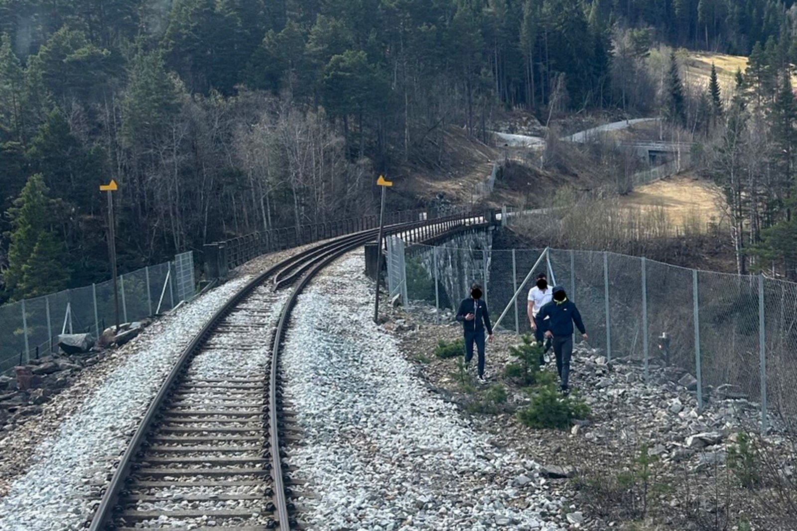 Tre personer mellom sporet og gjerdet med brua i bakgrunnen.