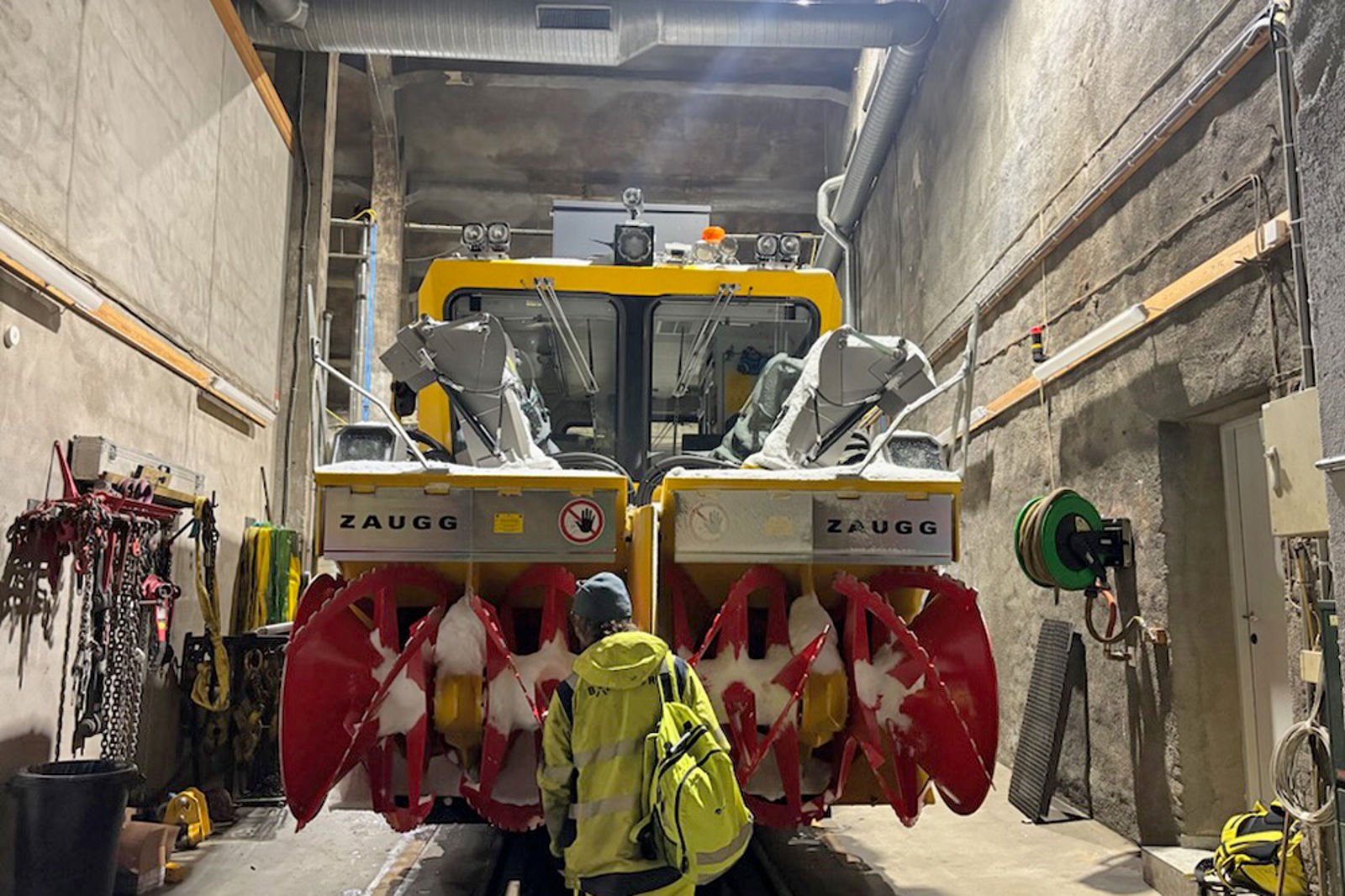 En skinnegående snøfreser parkert i lokstall. En person i forgrunnen blir liten i forhold