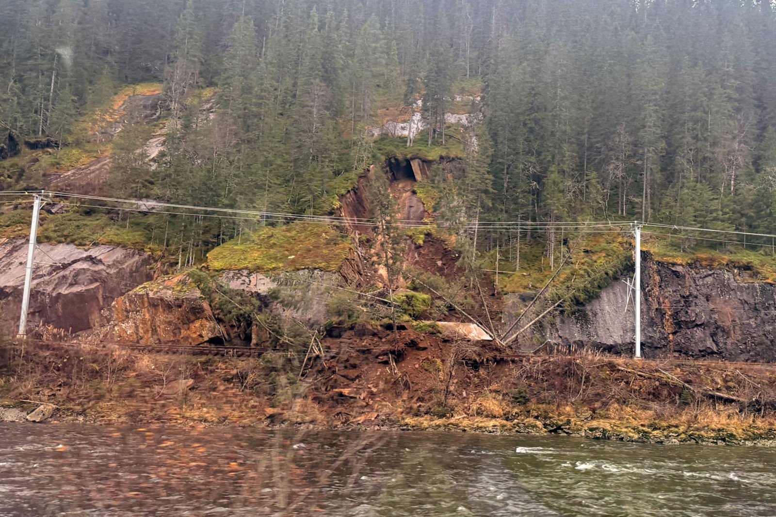 Bildet er tatt fra motsatt side av elva og viser at jord- og steinmasser har rast ut i sporet.