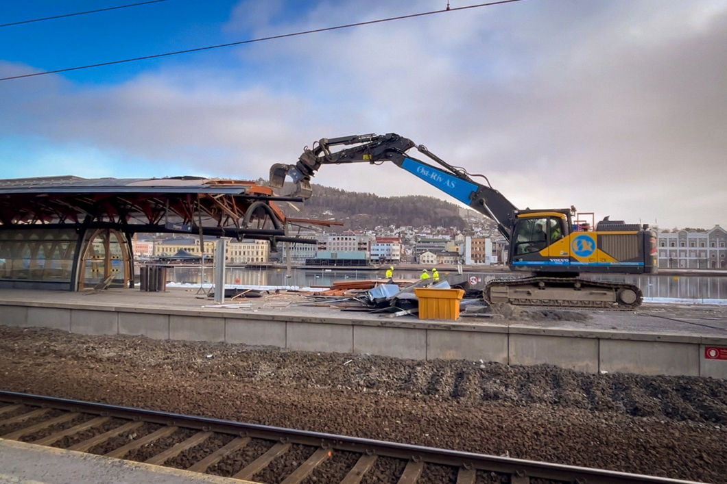 Anleggsmaskin river plattformtak på Drammen stasjon. Jernbanespor i forgrunn.