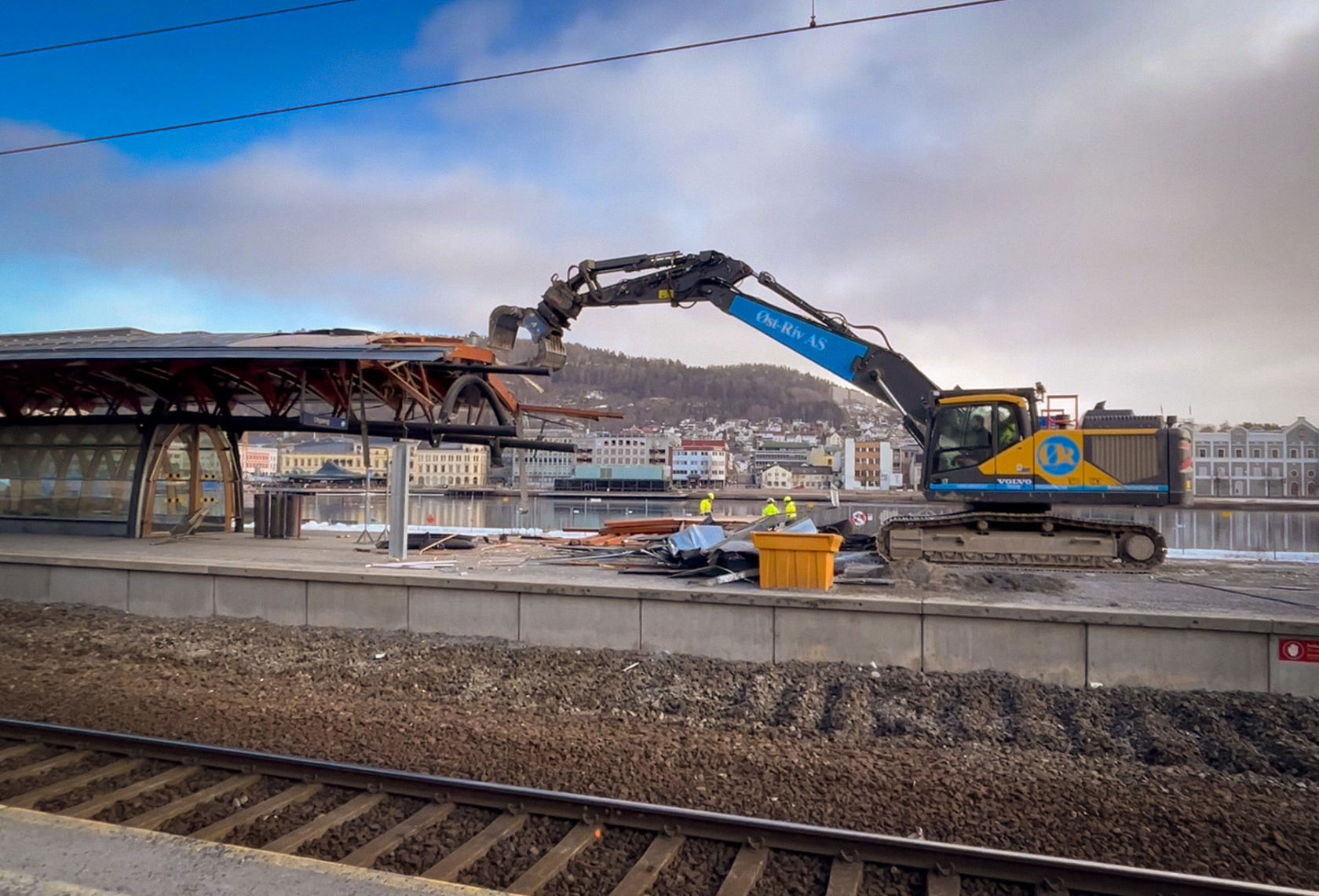 Anleggsmaskin river plattformtak på Drammen stasjon. Jernbanespor i forgrunn.
