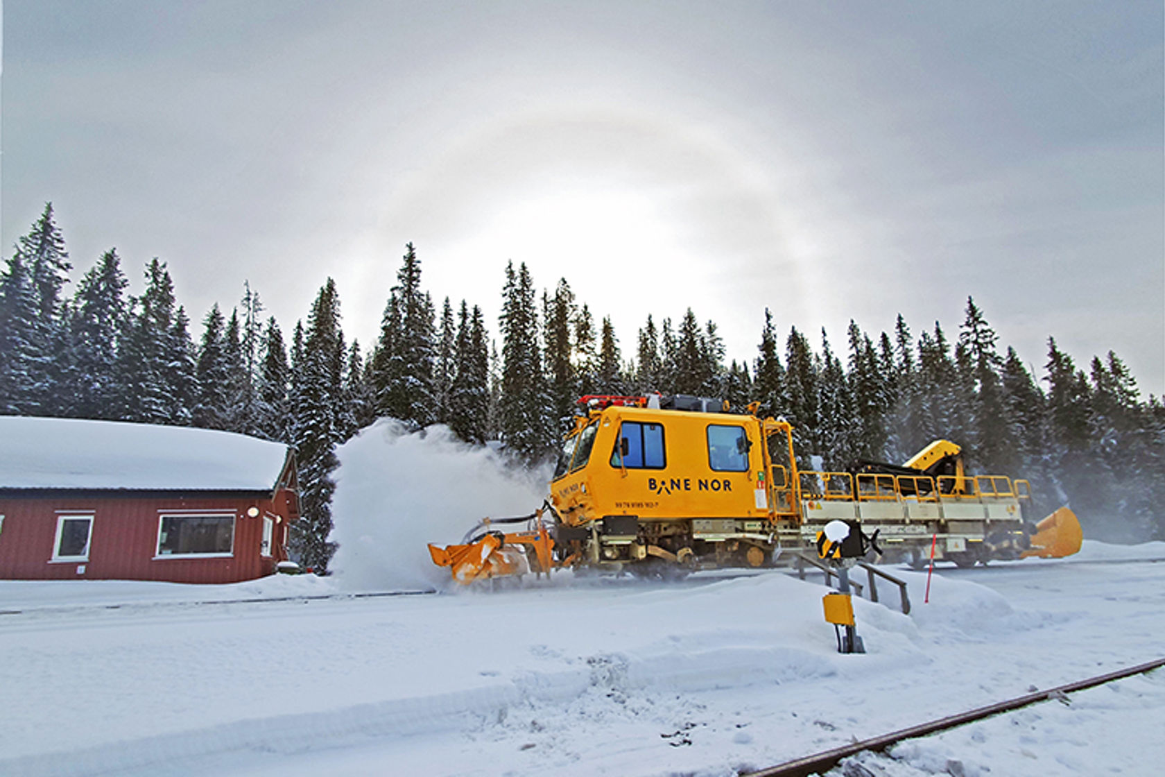Bilde av et gult arbeidstog som brøyter vekk snø fra skinnegangen.