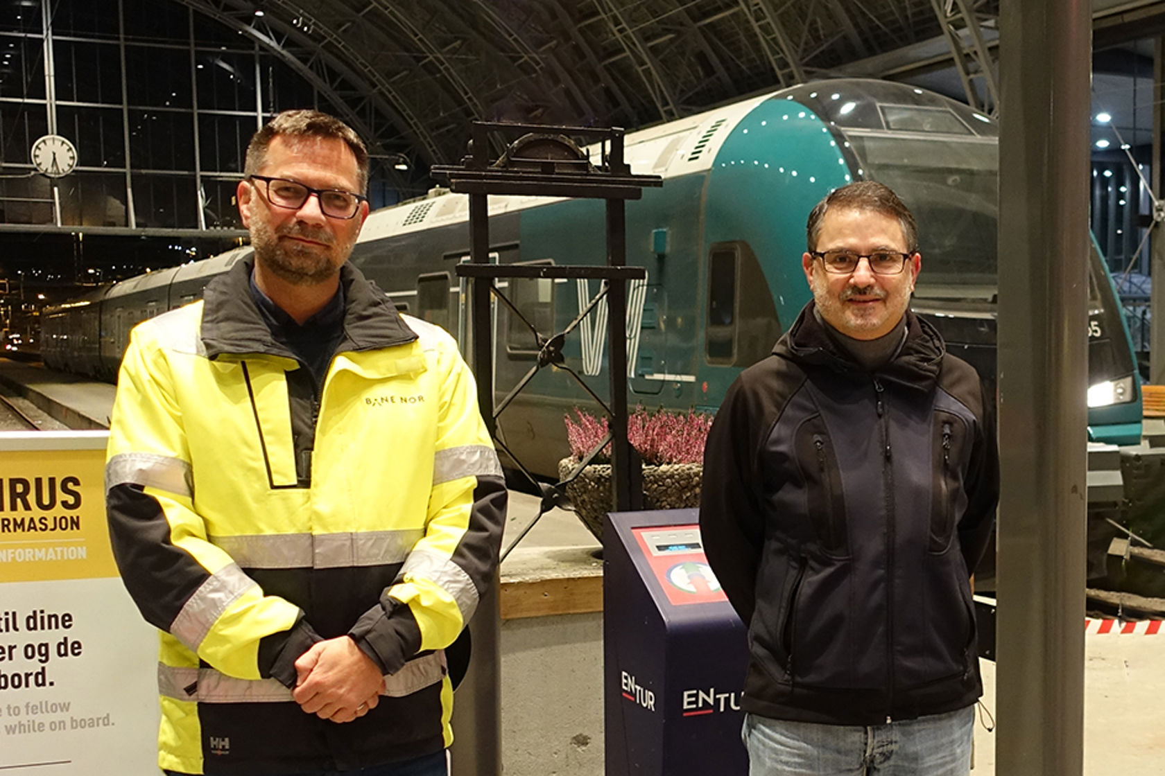 Bilde av to menn på Bergen stasjon, med et tog i bakgrunnen.