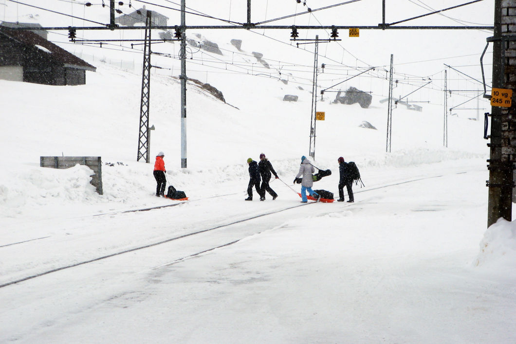 Folk som går over jernbanesporet, bærende på sekker, akebrett og ski, på Finse stasjon. 