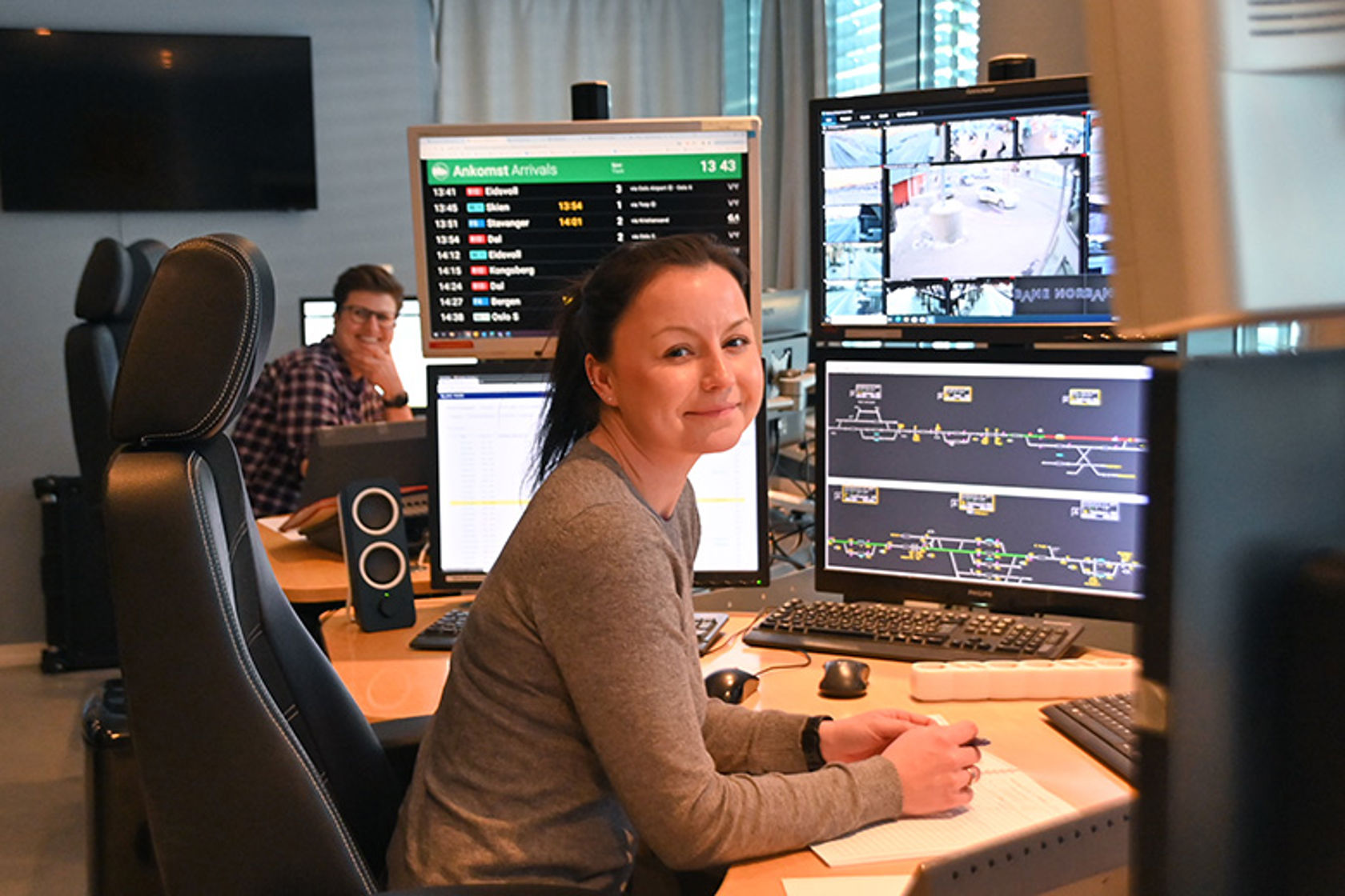 En kvinne sitter ved en arbeidspult med PC og flere skjermer.