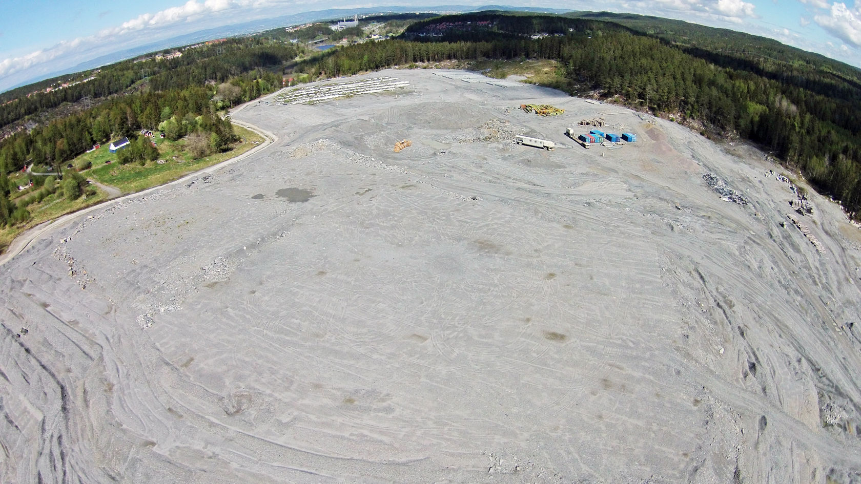 Dronebilde ovenfra av et stort område med grus og stein, omgitt av skog.