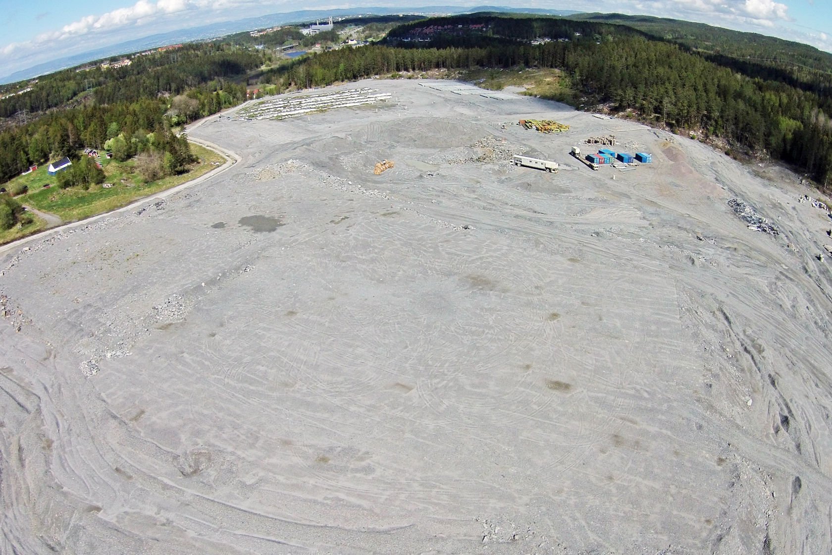 Dronebilde ovenfra av et stort område med grus og stein, omgitt av skog.
