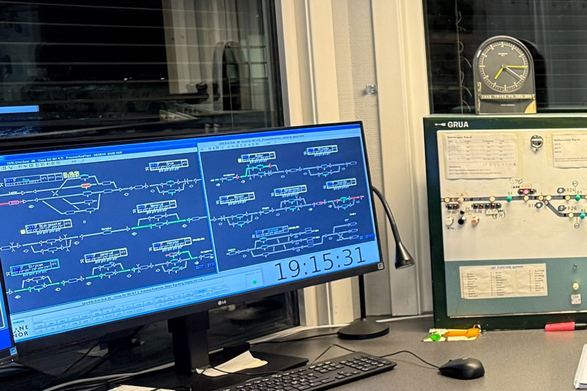 Azad sitter foran flere dataskjermer med systemer for en togleder og smiler til kamera