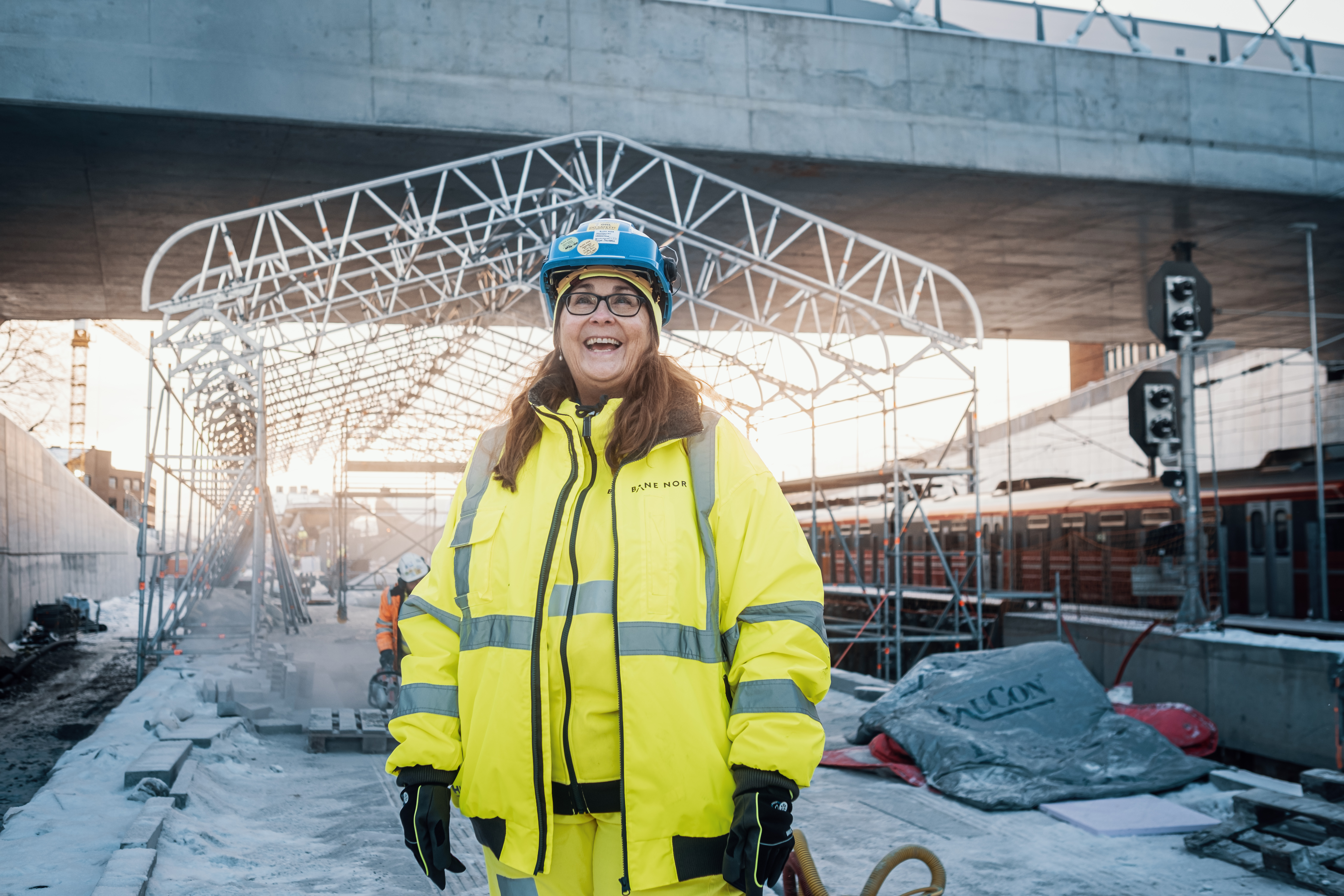 Smilende kvinnelig ansatt står foran byggeprosjekt - Follobanen