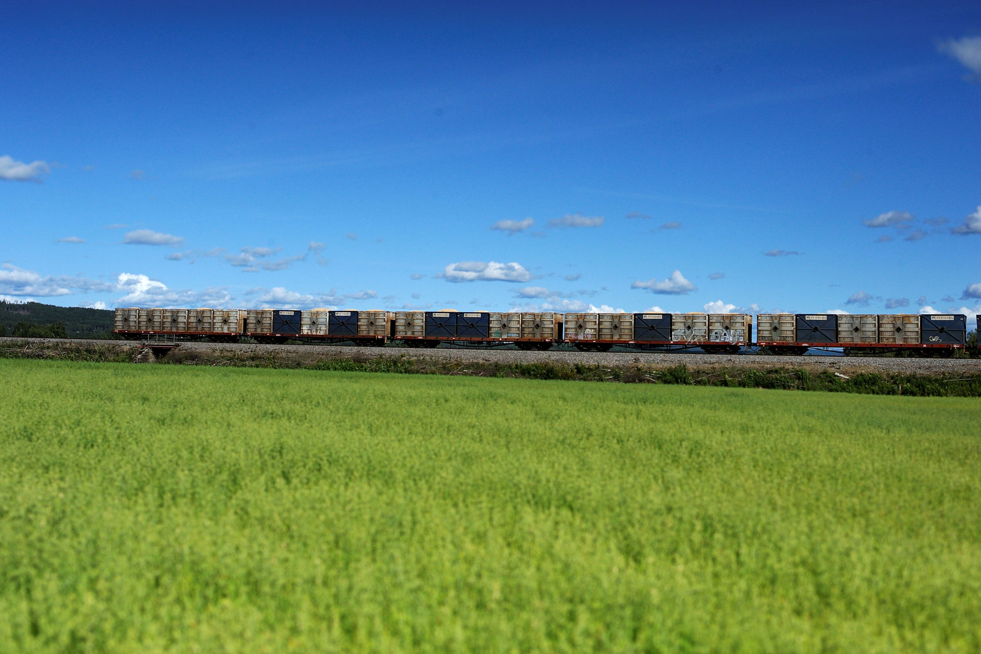 Godstransport på jernbaneskinne med grønt jorde i front og blå himmel